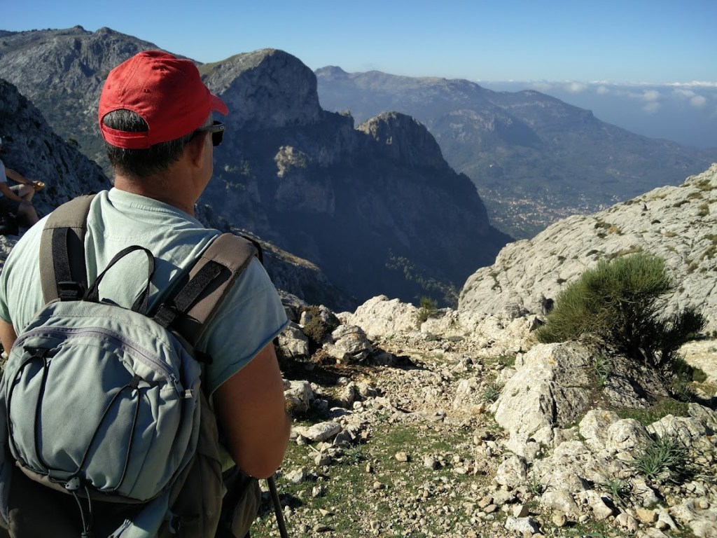 Un senderista con mochila observa el paisaje montañoso desde el Coll de ses Solanes, con vistas a valles y montañas en el fondo.