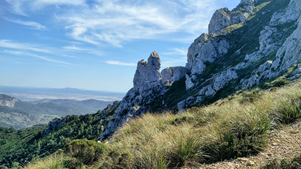 Vista del Peñasco llamado “Es Bisbe” cubiertas de vegetación con rocas prominentes en el paisaje y un cielo azul con nubes