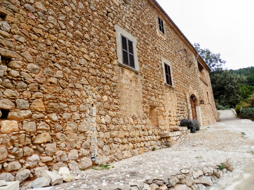 Vista lateral de la antigua casa de Son Serralta de Dalt con ventanas y una entrada, ubicada en un camino en una zona rural.