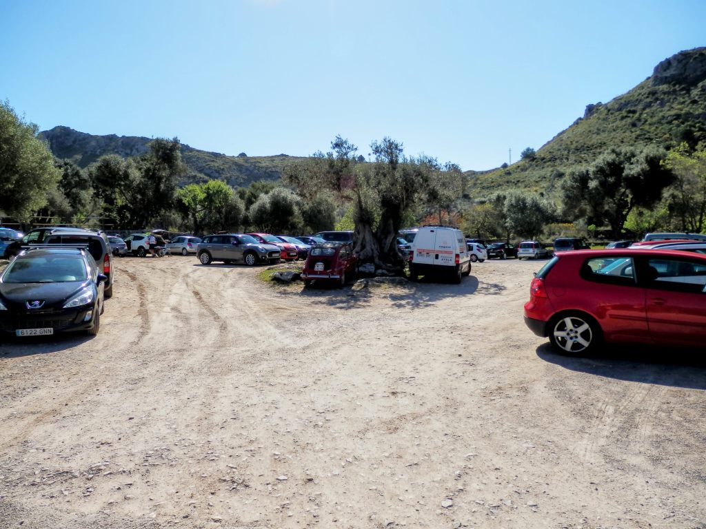 Aparcamiento de s’Alqueria Vella de Baix con numerosos coches en un entorno natural, rodeado de montañas y vegetación.