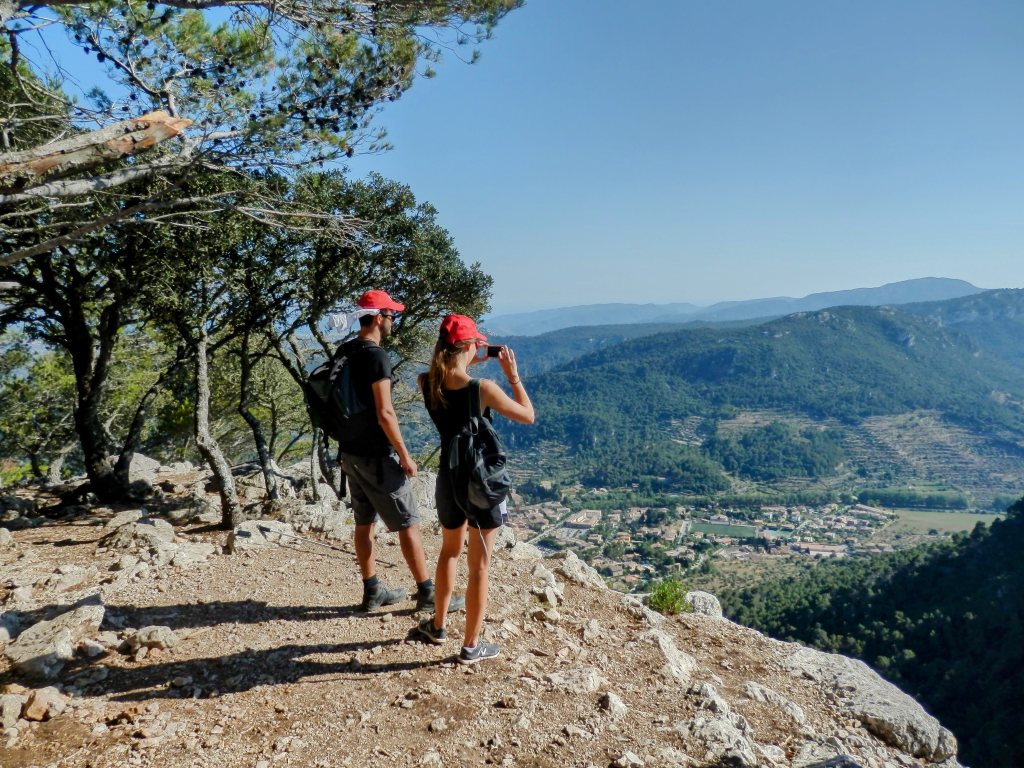 Dos excursionistas observando el paisaje desde el Mirador de sa Regata de les Onze en la Sierra de Tramuntana, con vistas a un valle y montañas en el fondo.