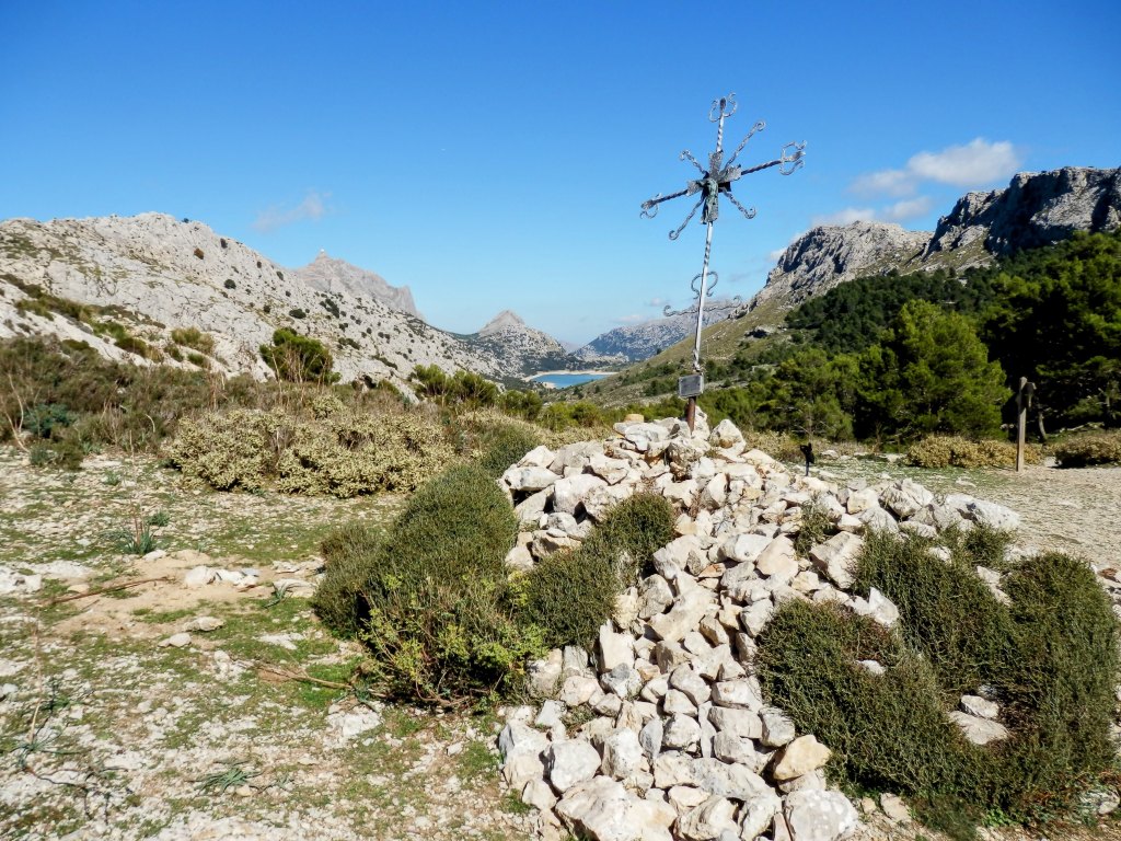 Vista panorámica desde el Coll de l’Ofre, con una cruz de piedra en primer plano, rodeada de montañas y vegetación, en la Serra de Son Torrella.