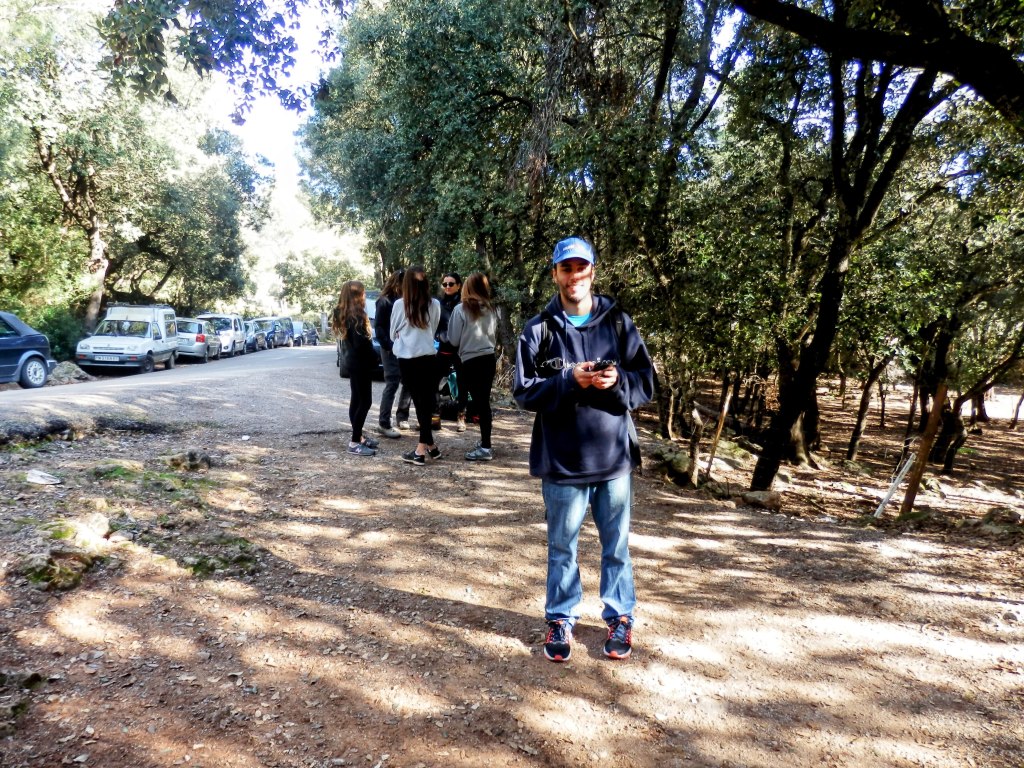 Grupo de personas en un sendero natural, con árboles a los lados y vehículos estacionados en la carretera cercana.