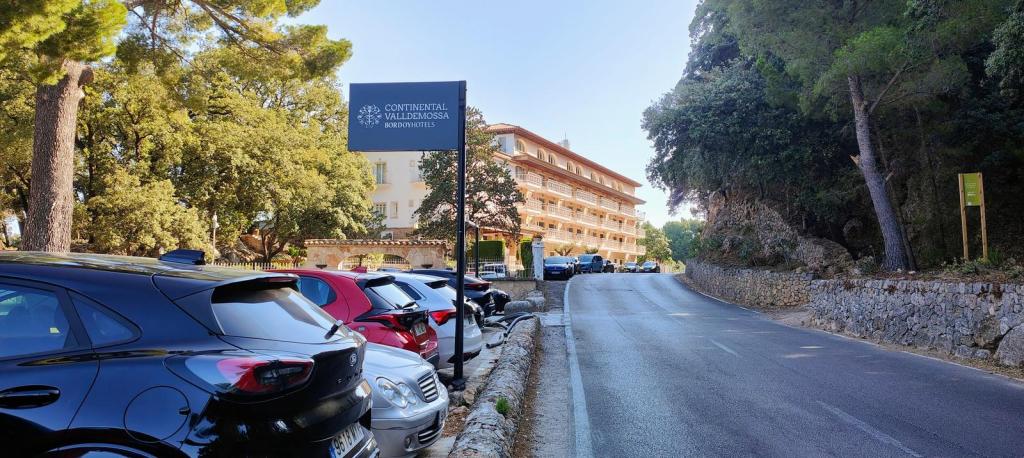 Vista del Hotel Continental en Valldemossa, rodeado de árboles y coches estacionados a lo largo de la carretera.
