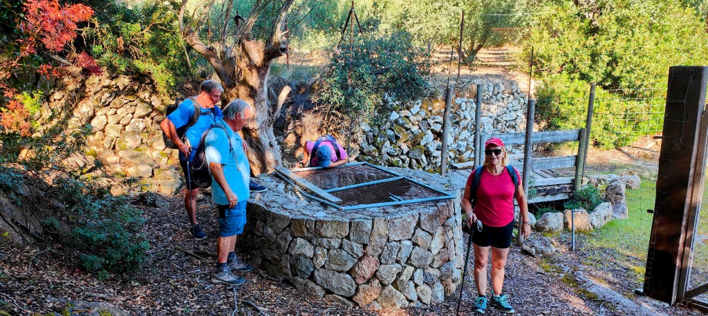 Grupo de personas observando una construcción de piedra circular con una tapa de rejilla en una ruta en la naturaleza.
