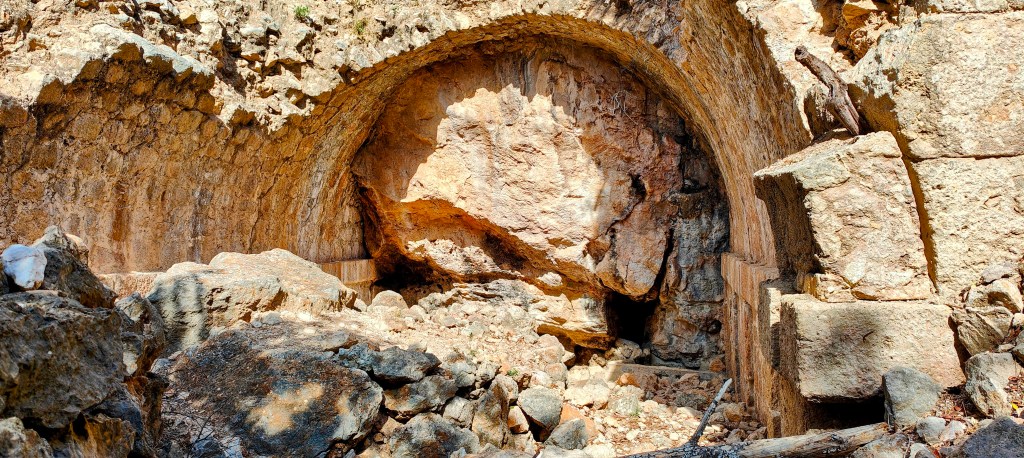 Vista de la Font de Son Verí en un entorno rocoso, con un arco tallado en la roca y escombros alrededor.