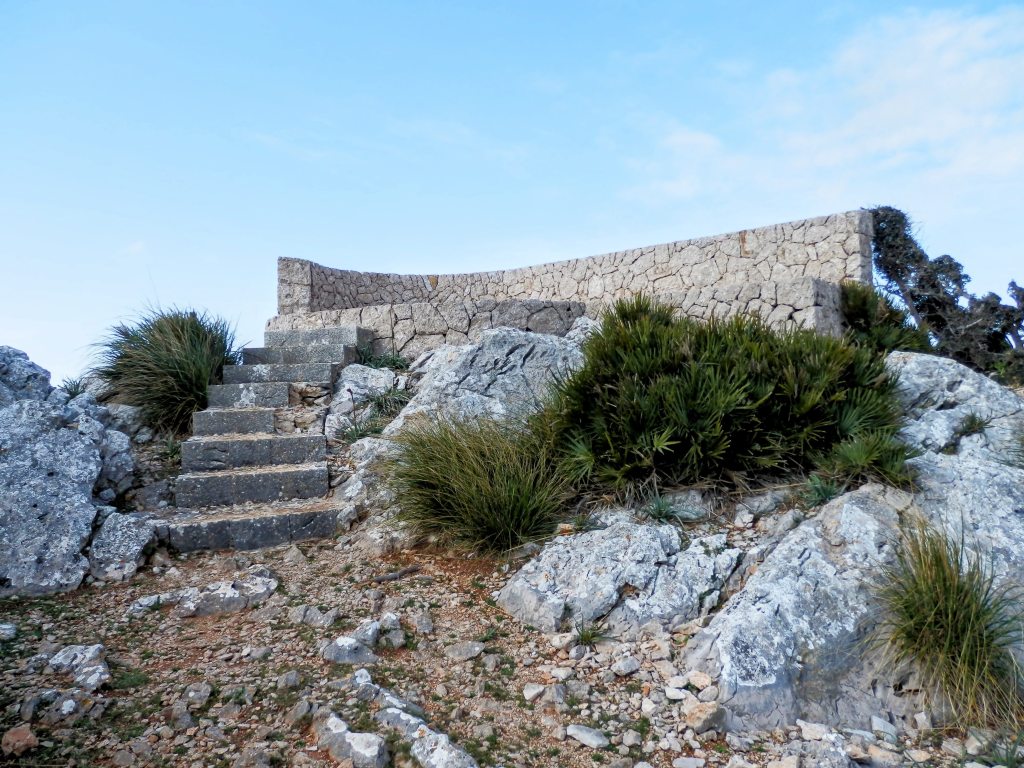 Escalera de piedra que conduce a un mirador en la cima del Puig d'en Farineta, con un muro de piedra de media altura y vegetación circundante.