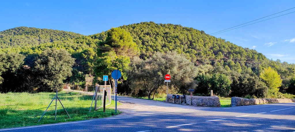 Vista de la intersección del Camí del Pinar de Canet y la carretera Ma-1120, con un paisaje montañoso de fondo y señalización vial visible.