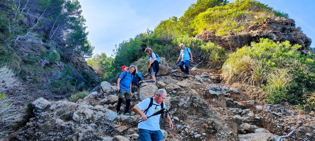 Grupo de senderistas descendiendo por un camino rocoso rodeado de vegetación en la Punta de Cas Taverner.