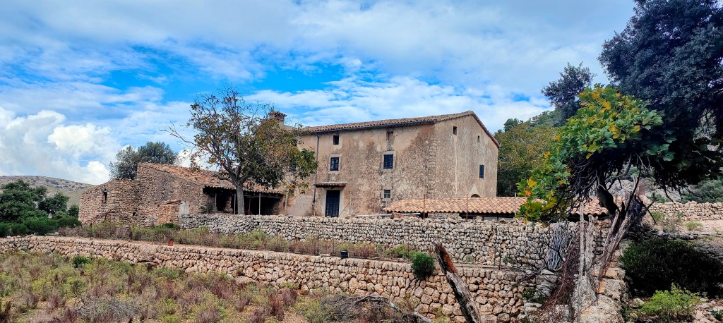 Vista de las Casas de Son Nebot en un entorno natural, con un cielo parcialmente nublado y vegetación alrededor.