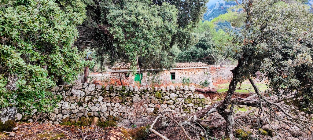 Vista de un antiguo edificio de piedra rodeado de vegetación y muros de piedra en un entorno natural.