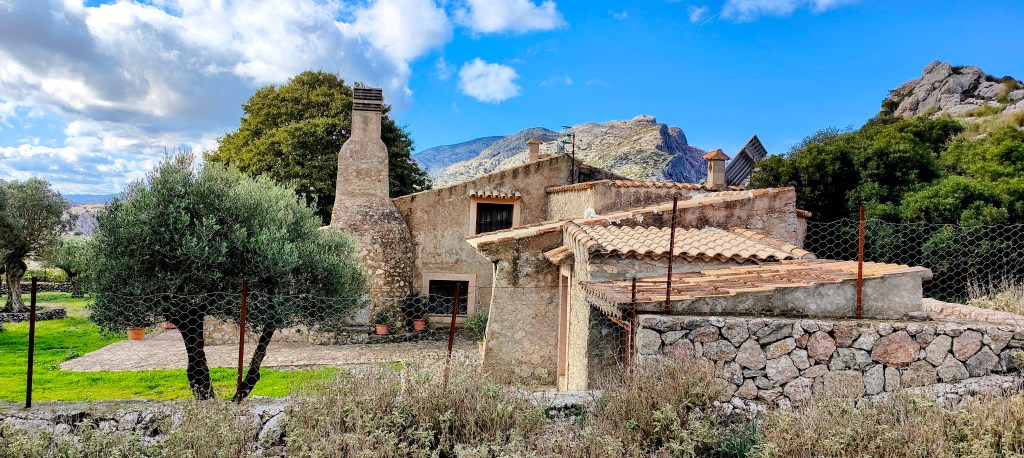 Vista de las casas de Sa Mola de piedra con un tejado de tejas, rodeada de vegetación, ubicada en un paisaje montañoso.