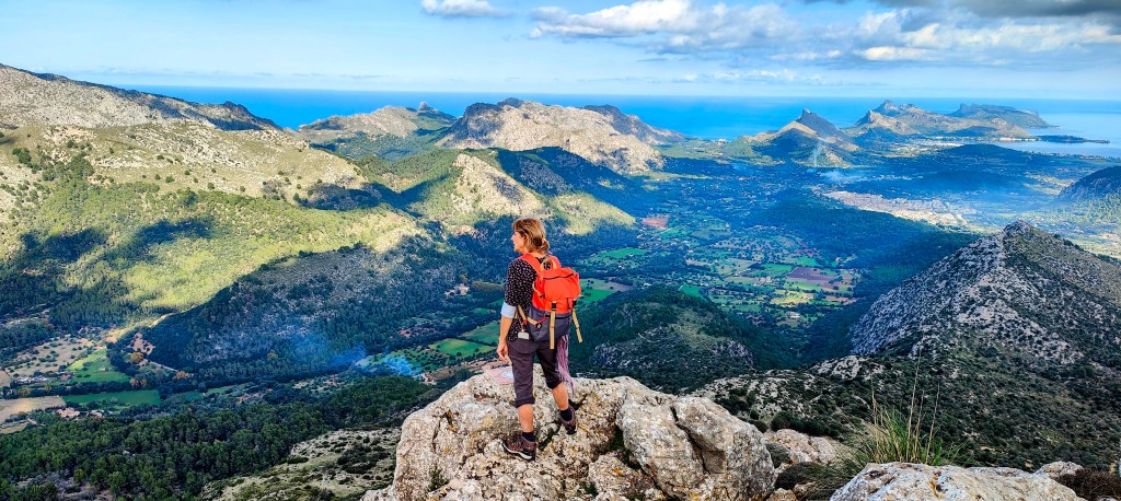 Vista panorámica desde la cima de la Cuculla de Fartàritx, donde una persona contempla el paisaje de montañas y el mar en el horizonte.