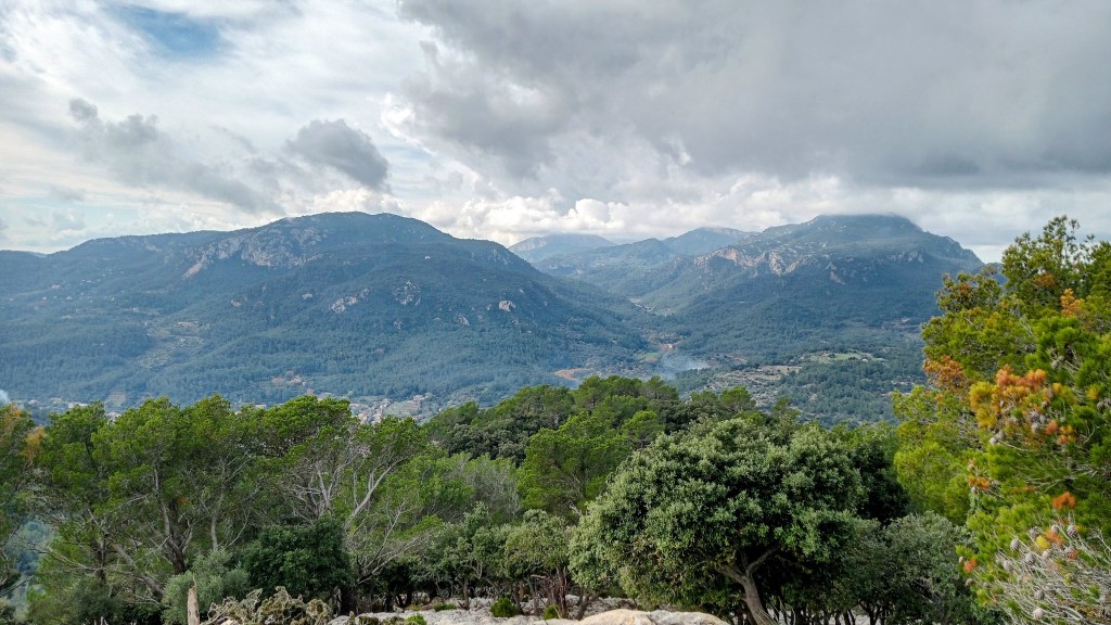 Vista panorámica de montañas y valles desde la cima de la Moleta de Son Cabaspre, con nubes en el cielo y vegetación en primer plano.