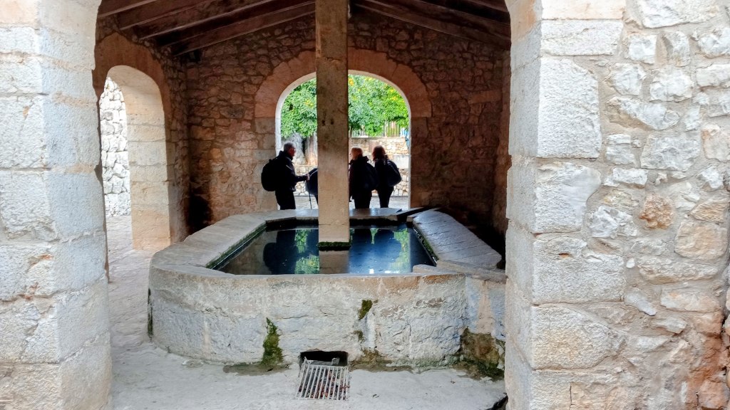 Vista interior de la Font de la Vila, un manantial de origen islámico con un antiguo sistema de riego, que presenta una estructura de piedra y un estanque de agua en el centro.