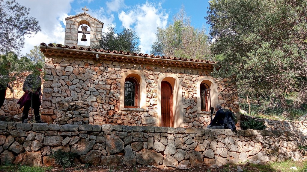 Ermita de la Reconciliació, una pequeña iglesia de piedra con campanario, rodeada de vegetación en un paisaje natural.