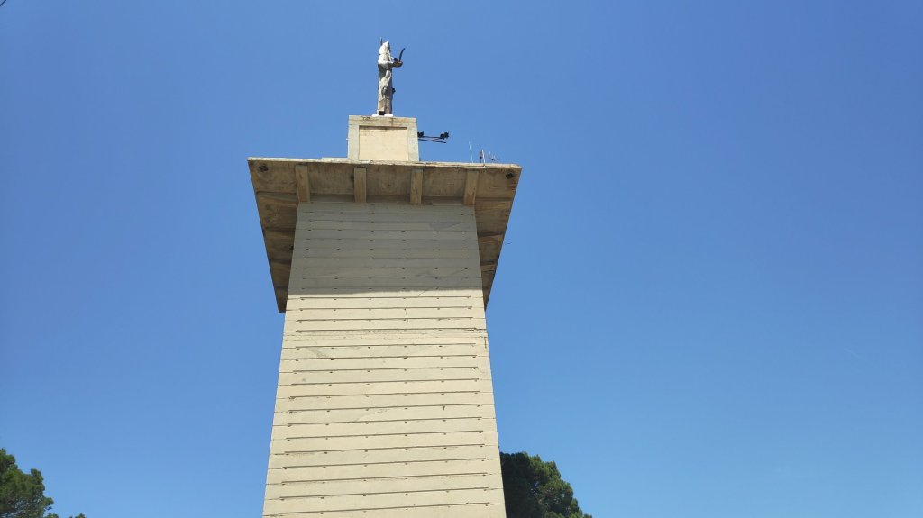 Monumento de Na Burguesa en Calviá, Mallorca, con una escultura de Nuestra Señora de la Pau en su parte superior, bajo un cielo azul.