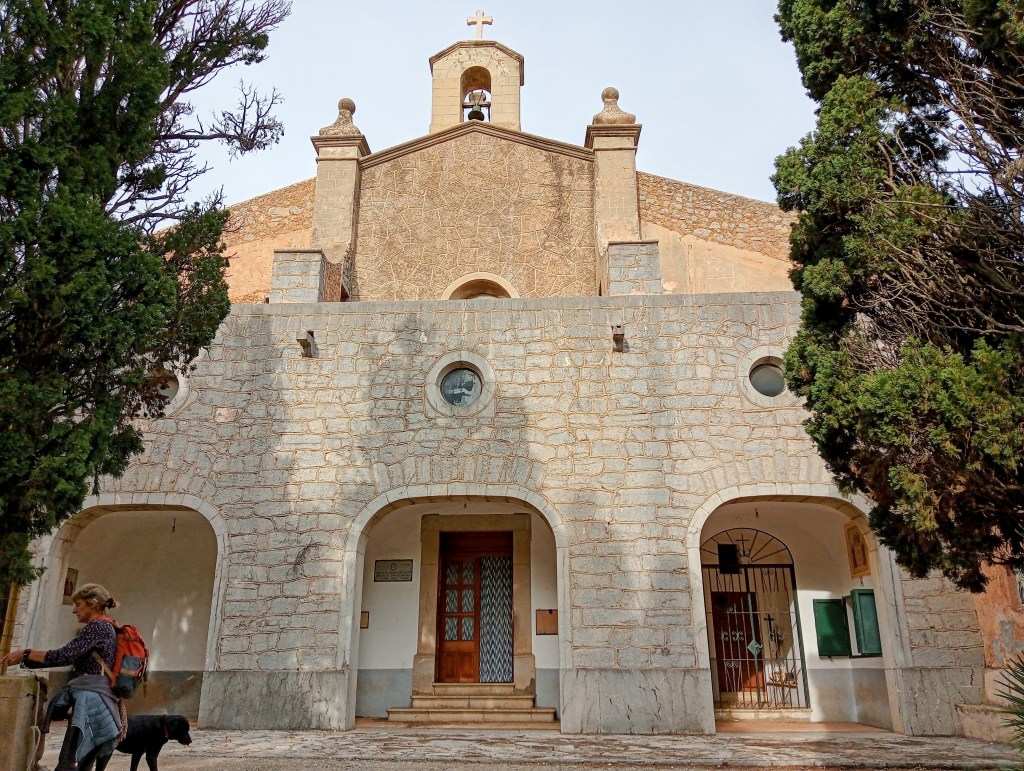 Ermita de Betlem, una construcción sencilla con arcos en la entrada, rodeada de cipreses y un paisaje montañoso.