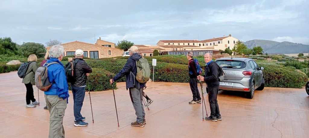 Grupo de personas preparándose para iniciar una caminata en el aparcamiento del Carrossa Hotel & Spa, en un paisaje de Mallorca con vegetación y montañas al fondo.