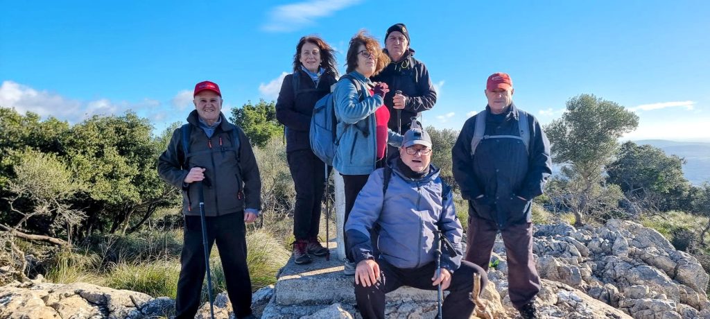 Grupo de seis personas posando en la Cima del Puig des Boixos, con árboles y cielo despejado de fondo.