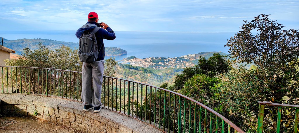 Hombre con mochila tomando fotos desde el Mirador de ses Barques, de un paisaje montañoso con vista al mar.