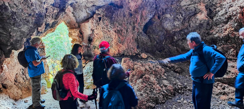 Grupo de personas explorando una cueva con formaciones rocosas visibles y una salida iluminada en el fondo.