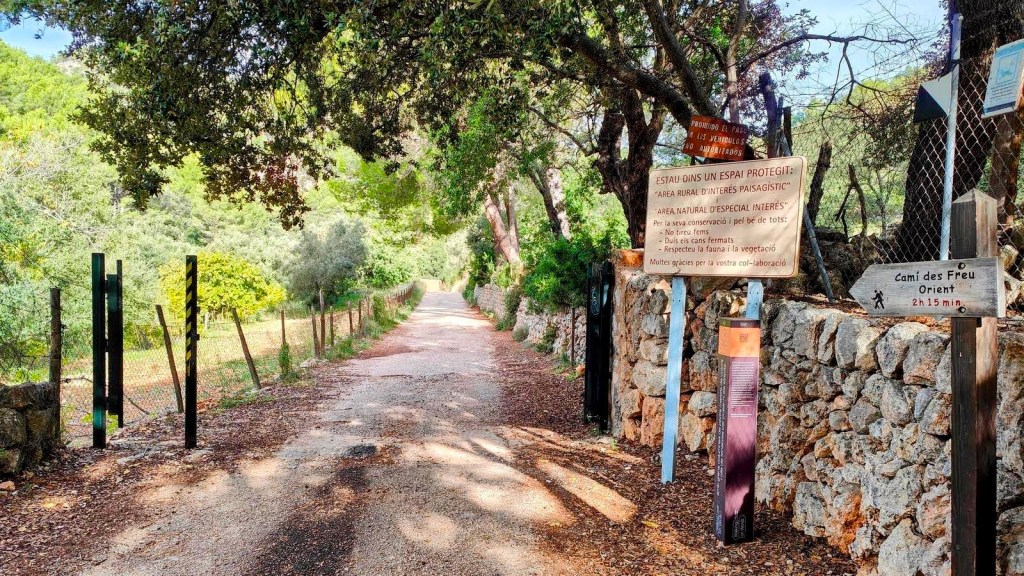 Camino rural en un área protegida, con señales informativas y cercas de alambre que bordean el camino, rodeado de árboles y vegetación.