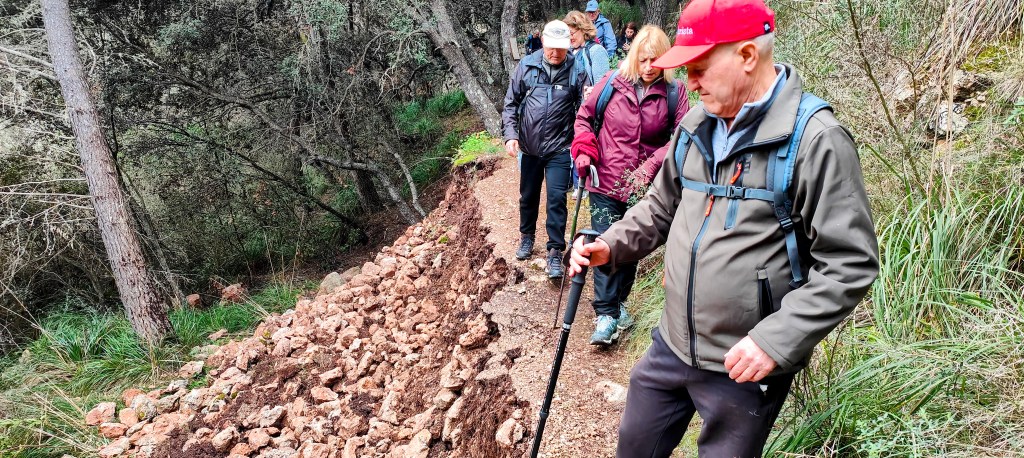 Grupo de senderistas caminando por un sendero de tierra, con rocas y vegetación a los lados.