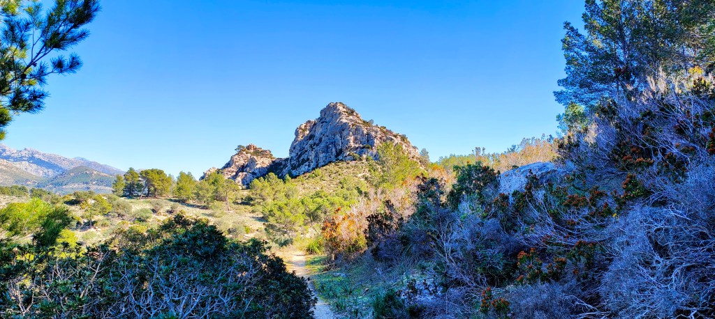 Vista panorámica de Es Tres Picons, un paisaje montañés con rocas y vegetación, en un día despejado.