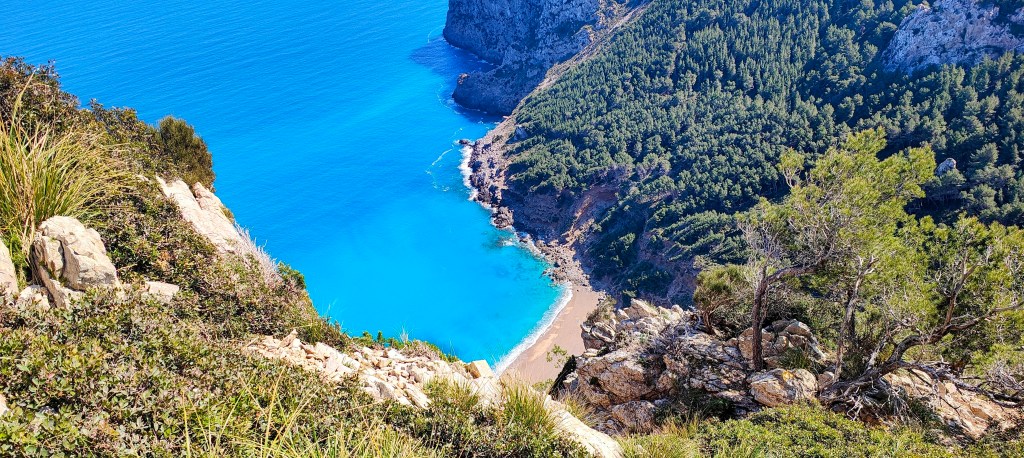 Vista panorámica de una playa de aguas turquesas desde un acantilado, rodeada de vegetación y montañas.