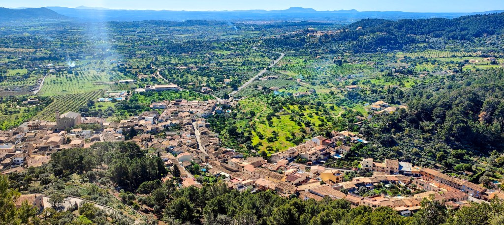 Vista aérea de un paisaje rural, mostrando un pueblo rodeado de campos y montañas en el fondo.