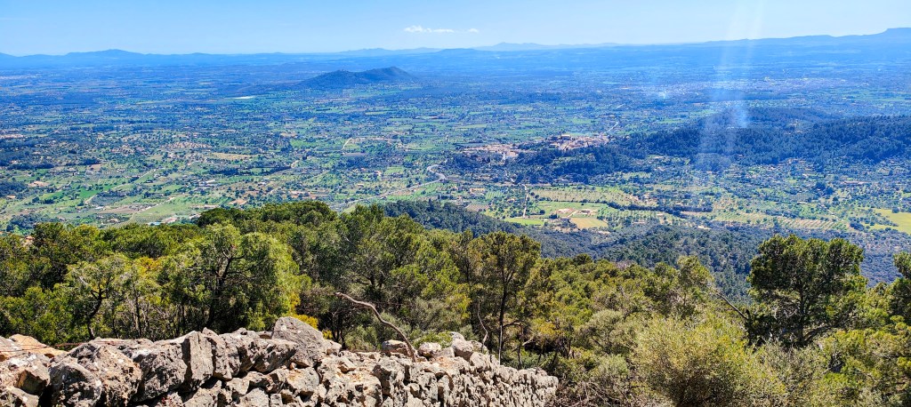 Vista panorámica de un paisaje montañoso con valles verdes, árboles y un cielo despejado.