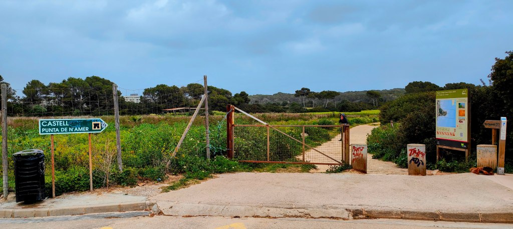 Entrada al camino hacia Punta de n'Amer con un cartel que indica 'Castell' y un campo verde al fondo.