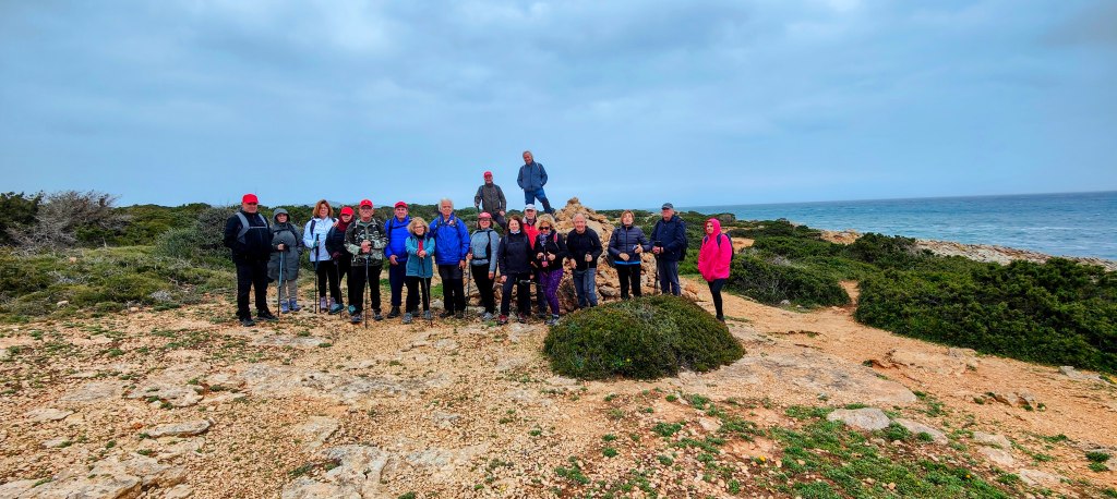 Grupo de personas de pie en una costa rocosa, con mar de fondo y cielo nublado.