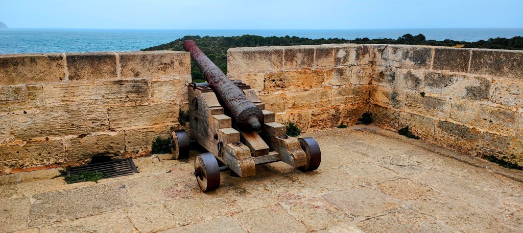 Un cañón antiguo en una fortaleza con vista al mar y la vegetación circundante.